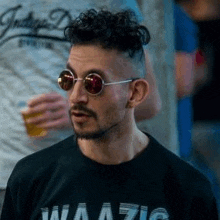 a man wearing sunglasses and a black shirt is standing in front of a group of people .