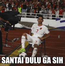 a soccer player with the number 7 on his jersey sits on a chair with a soccer ball in front of him