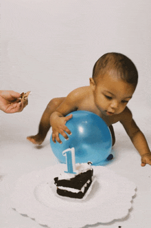 a baby crawls next to a blue balloon and a cake with the number 1 on it