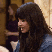 a woman with long dark hair and bangs is smiling while sitting at a table in a living room .