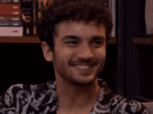 a man with curly hair and a beard is smiling in front of a bookshelf with books on it .