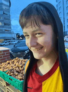 a young boy wearing a red and yellow nike shirt smiles in front of a green basket of potatoes