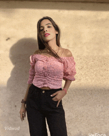 a woman in a pink off the shoulder top stands in front of a wall