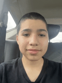 a young boy with a shaved head is sitting in a car and smiling for the camera .