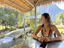 a woman in a bikini sits at a table looking out over a river