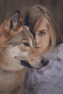 a woman in a white lace top holds a brown wolf