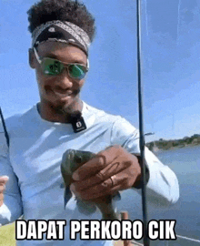 a man wearing sunglasses is holding a fish in his hand .