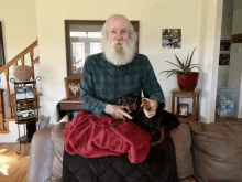 a man with a beard is sitting on a couch holding a small dog