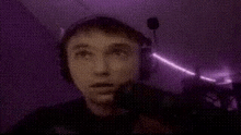 a man wearing headphones is standing in a dark room with a purple light coming from the ceiling .