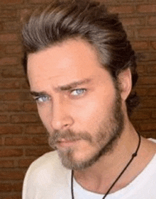 a man with a beard and blue eyes is wearing a white shirt .