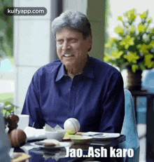 a man in a blue shirt is sitting at a table with a bowl of food and a ball .