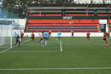 a group of soccer players are playing on a field with a sign that says sport in the background