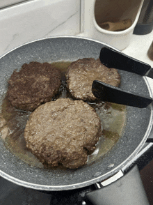 three hamburger patties are cooking in a frying pan with tongs