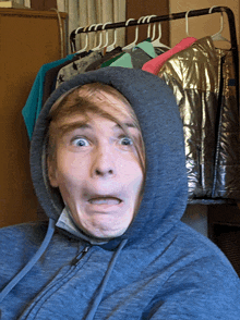 a man wearing a hoodie is making a funny face in front of a rack of clothes