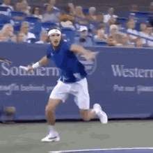 a man in a blue shirt and white shorts is running on a tennis court while holding a tennis racket .