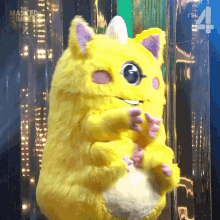 a yellow stuffed animal from the masked singer is sitting in front of a green screen