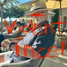 a man in a hat sits in a chair with the word violence written in red across his face