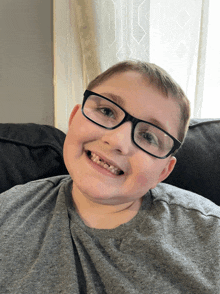 a young boy wearing glasses and a grey shirt is smiling