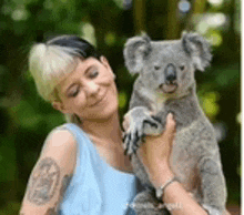 a woman is holding a koala bear in her arms in a forest .