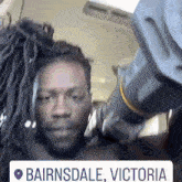 a man with dreadlocks is in a car with a sign that says ' bairnsdale victoria ' on it