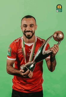 a man in a red shirt holds a trophy and a soccer ball