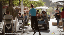 a woman in a blue shirt is standing in front of a golf cart with the nbc logo in the corner