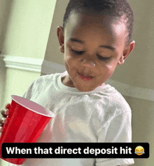 a young boy holding a red cup with the words when that direct deposit hit