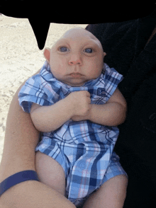 a baby wearing a blue and white plaid shirt with the letter s on it is being held by someone