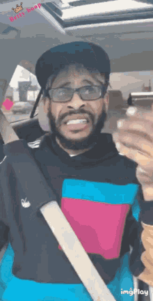 a man with a beard wearing glasses and a hat is in a car with a belt around his waist .