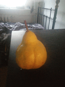 a pear with a red stem sits on a desk in front of a bed