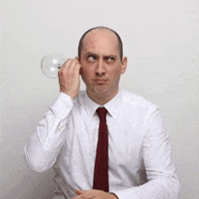 a man wearing a white shirt and red tie is holding a light bulb to his ear