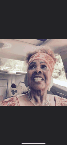 a woman wearing a bandana and a necklace is smiling in a car