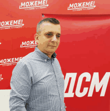 a man stands in front of a red wall that says " можеме " on it