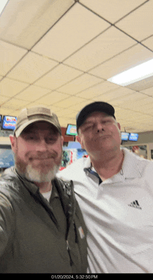 two men are posing for a picture in a bowling alley and one is wearing a white adidas shirt