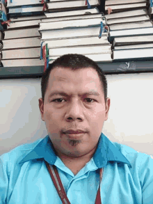 a man in a blue shirt with a lanyard around his neck is standing in front of a row of books