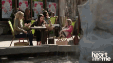 a group of women sit at a table in front of a fountain sponsored by super channel heart and home