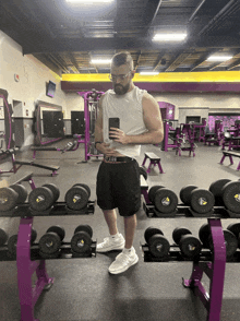 a man takes a selfie in a gym with purple dumbbells