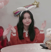 a girl wearing a bunny ear headband is sitting at a table with her hands in the air .