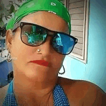 a woman wearing sunglasses and a green bandana is taking a selfie with her phone .