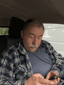 a man with a mustache is sitting in a car looking at his phone