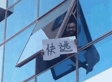 a man is peeking out of a window holding a sign in a foreign language .