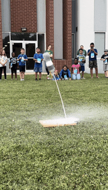 a group of children are standing in the grass watching a rocket launch