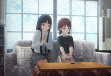 two anime girls are sitting on a couch looking at a television