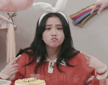 a woman wearing bunny ears is pointing at herself in front of a birthday cake