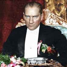 a man in a tuxedo and bow tie sits at a table with flowers