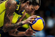 a woman with a tattoo on her arm holds a mikasa volleyball in her hand