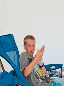 a young boy is sitting in a blue chair looking at his cell phone