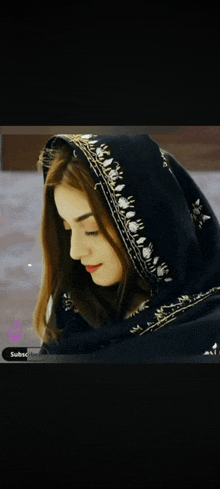 a woman wearing a black scarf with gold embroidery on the hood