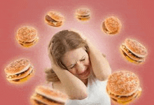 a woman is covering her ears in front of a bunch of hamburgers .