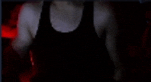 a man in a black tank top is standing in a dark room with a red light behind him .